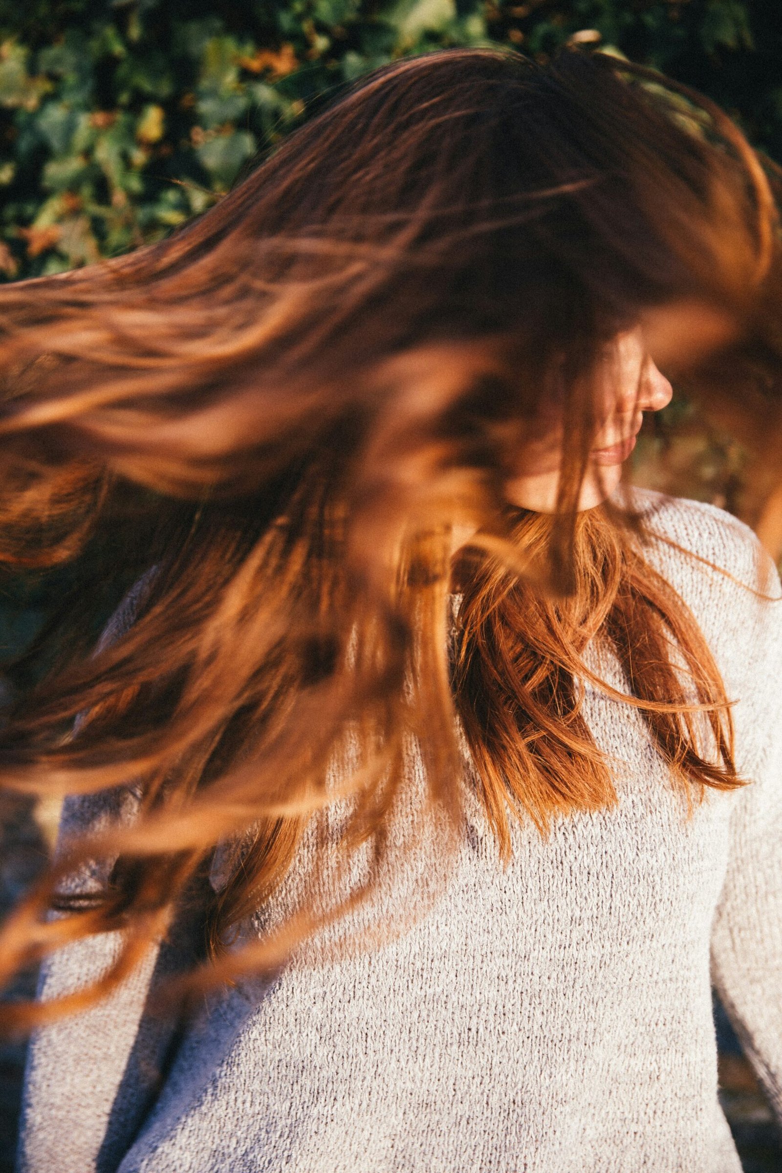 A woman in dusk light shakes her long hair implying motion or dance.